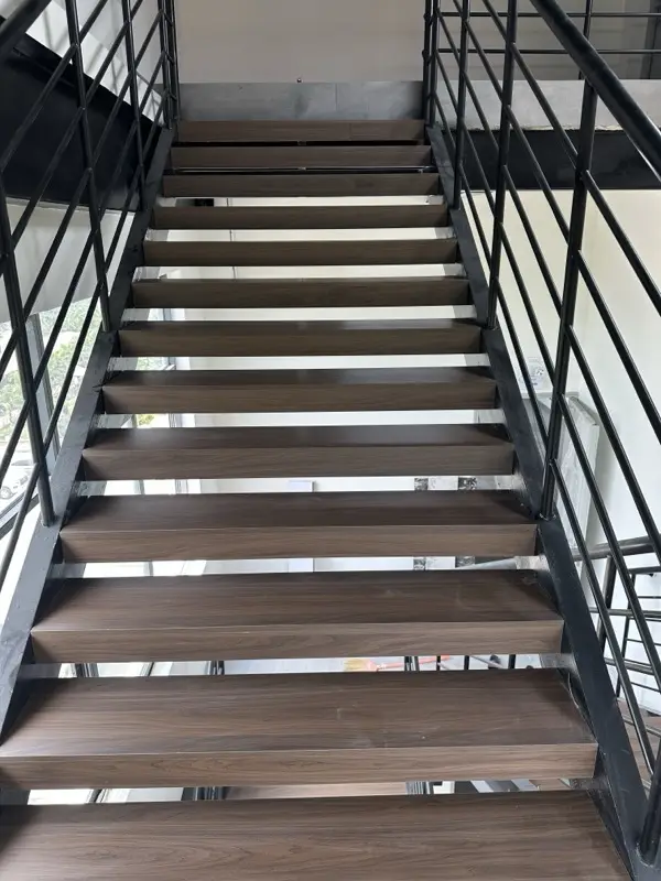 Cầu thang khung sắt sơn đen, mặt bậc vân gỗ tối, lan can thanh ngang