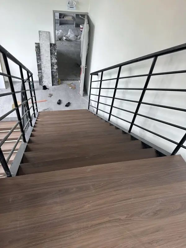 Cầu thang nhìn từ trên xuống, mặt bậc vân gỗ, tầng trên còn đang thi công