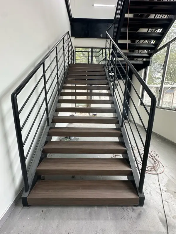 Cầu thang nhìn từ chân, mặt bậc vân gỗ tối, lan can sắt đen hai bên