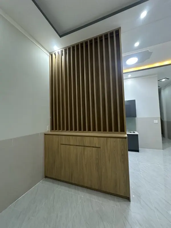Vách ngăn lam gỗ đứng trên tủ thấp vân gỗ, ngăn phòng khách với khu bếp phía sau