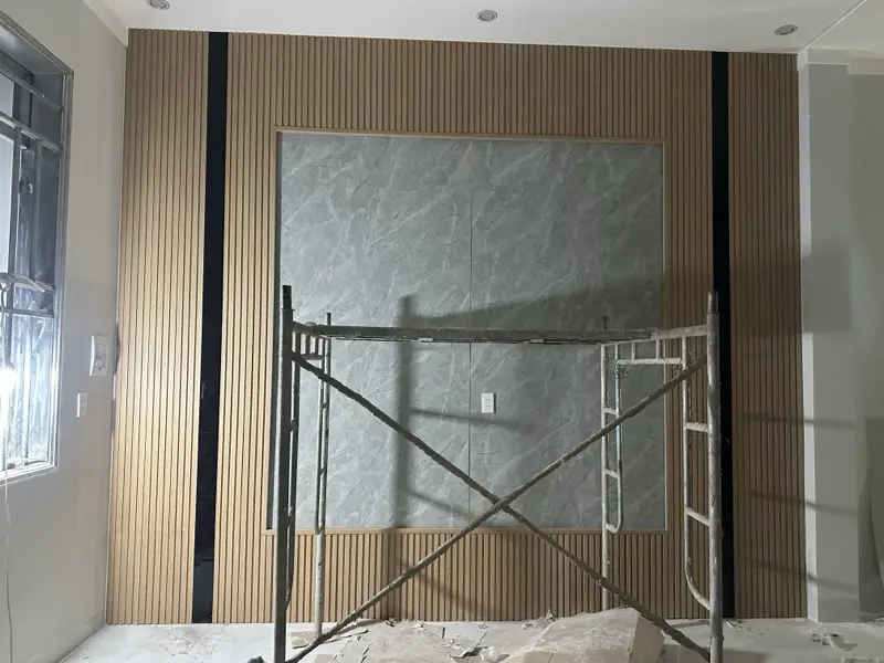 Vách lam gỗ và khung vân đá đang thi công, giàn giáo còn dựng trước tường