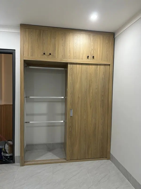 Tủ áo kịch trần vân gỗ màu sáng, cánh lùa mở một bên thấy thanh treo, tầng trên cánh mở