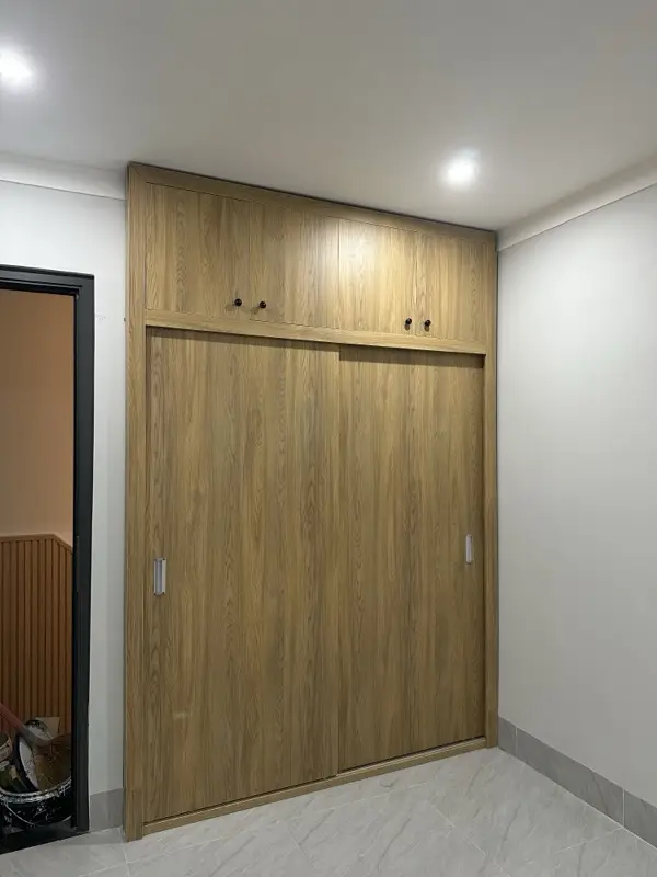 Tủ áo cánh lùa vân gỗ màu sáng đóng kín, tay nắm dọc