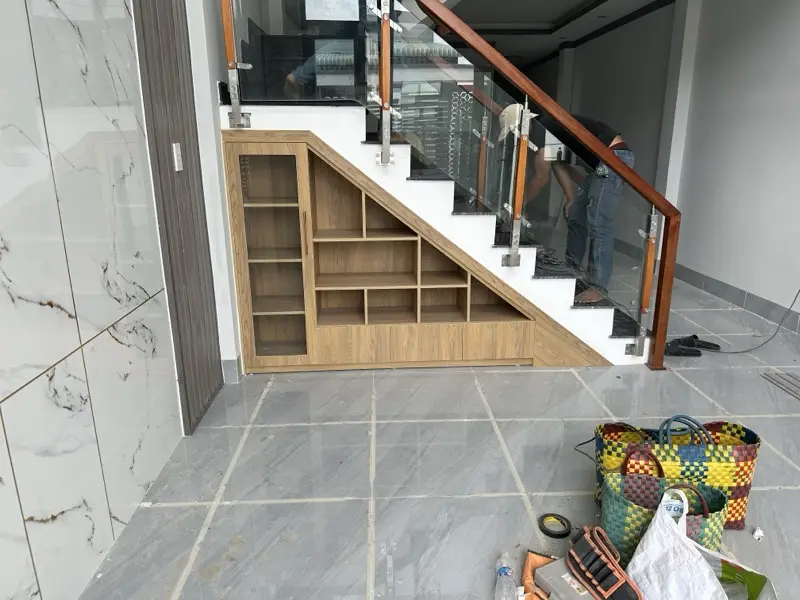Kệ gầm cầu thang vân gỗ màu sáng, ô mở và tủ cánh chạy theo độ dốc bậc thang