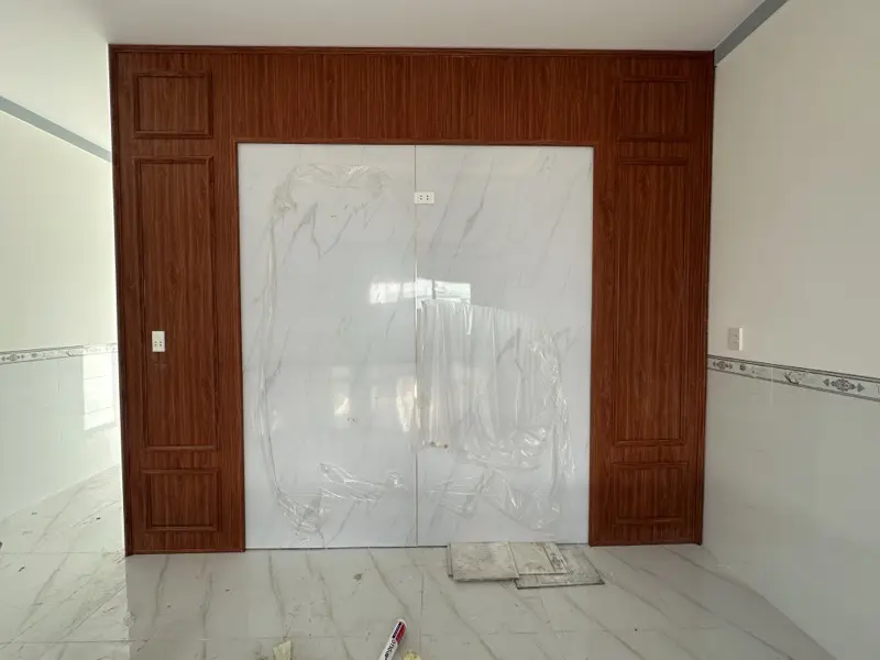 Vách ốp gỗ màu cánh gián làm khung quanh mảng vân đá trắng còn màng bảo vệ
