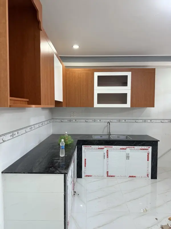 Tủ bếp trên vân gỗ có hai ô cánh kính khung trắng, mặt bếp đá đen
