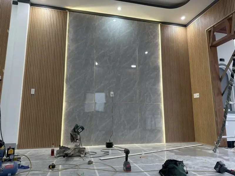 Vách tivi đang thi công: đã ốp PVC vân đá và lam, máy cắt và dụng cụ còn trên sàn
