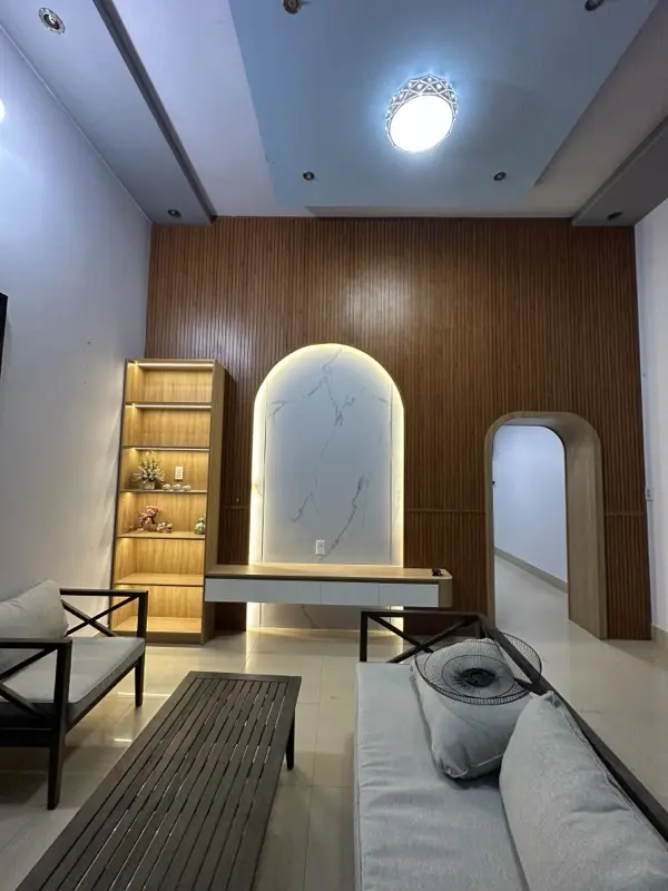 Toàn cảnh phòng khách: tường lam vân gỗ, vòm vân đá sáng đèn, cửa vòm ốp gỗ dẫn vào trong